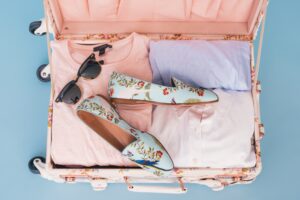 Pink and blue themed clothes and shoes in suitcase.